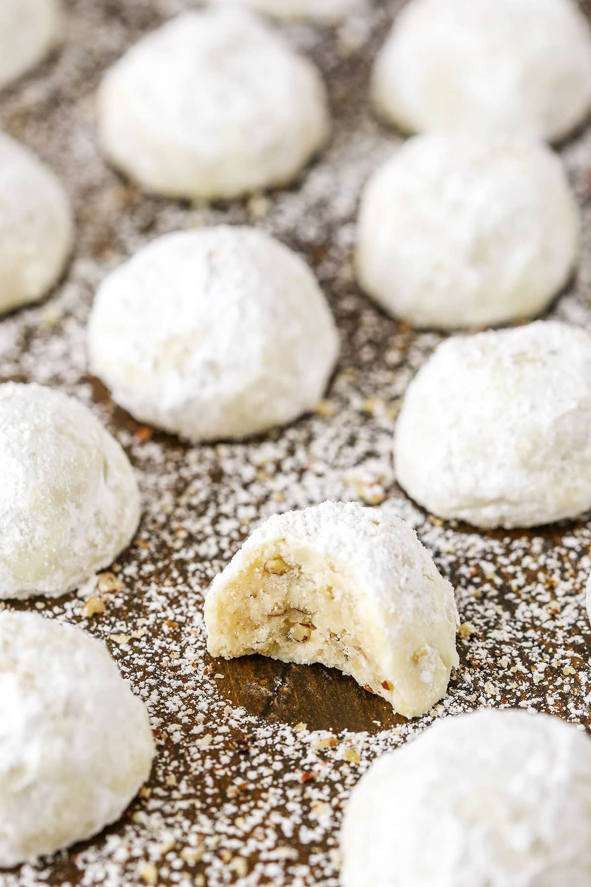 Russian Tea Cakes spread out evenly on a wooden board with one missing a bite and coated in powdered sugar