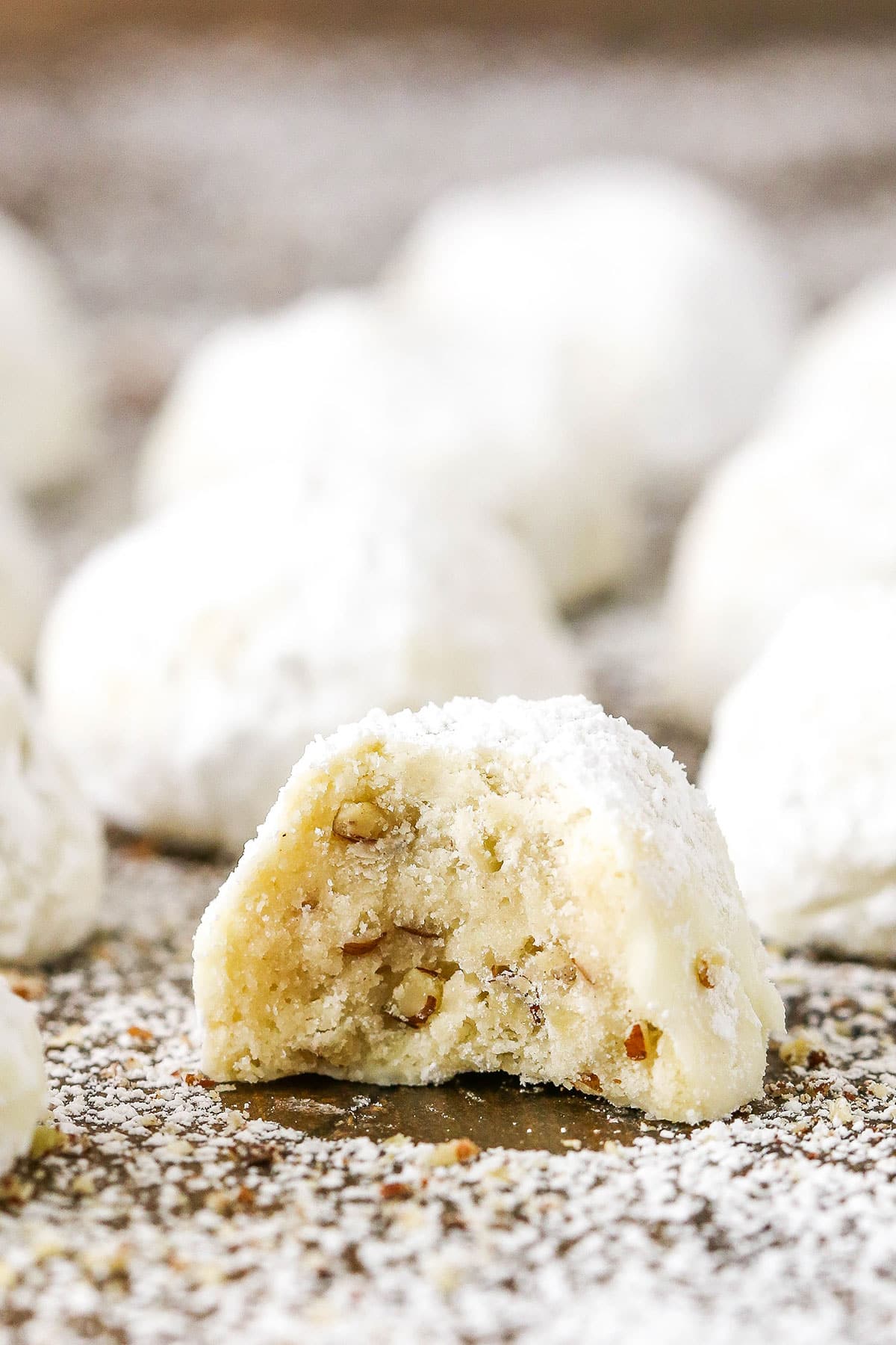 A Russian Tea Cake with a bite removed surrounded by mare Russian Tea Cakes on a wooden board and coated in powdered sugar