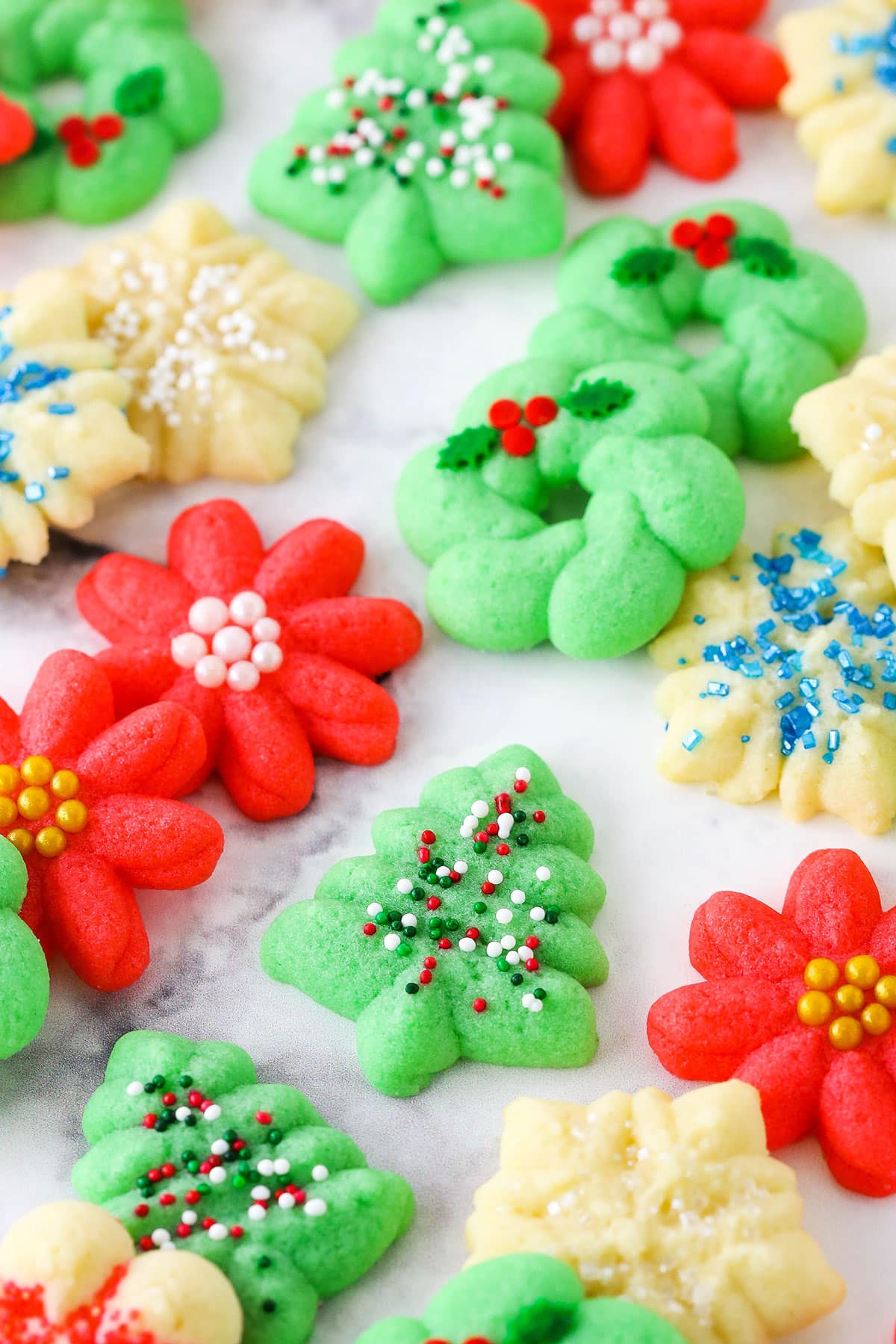Red flower, white snowflake and green Christmas tree Spritz Cookies spread out over a white table top