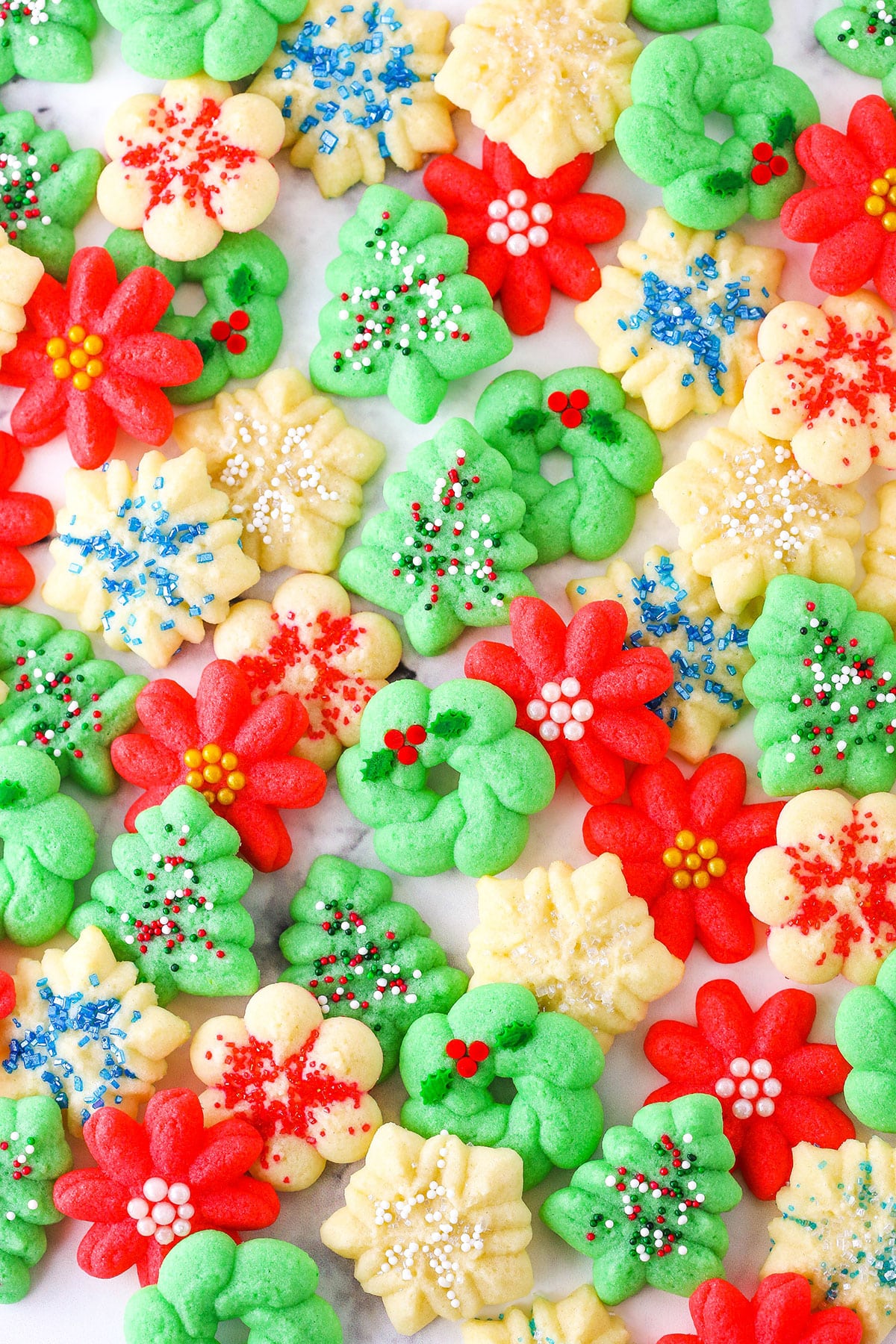 Red flower, white snowflake and green Christmas tree Spritz Cookies spread out over a white table top