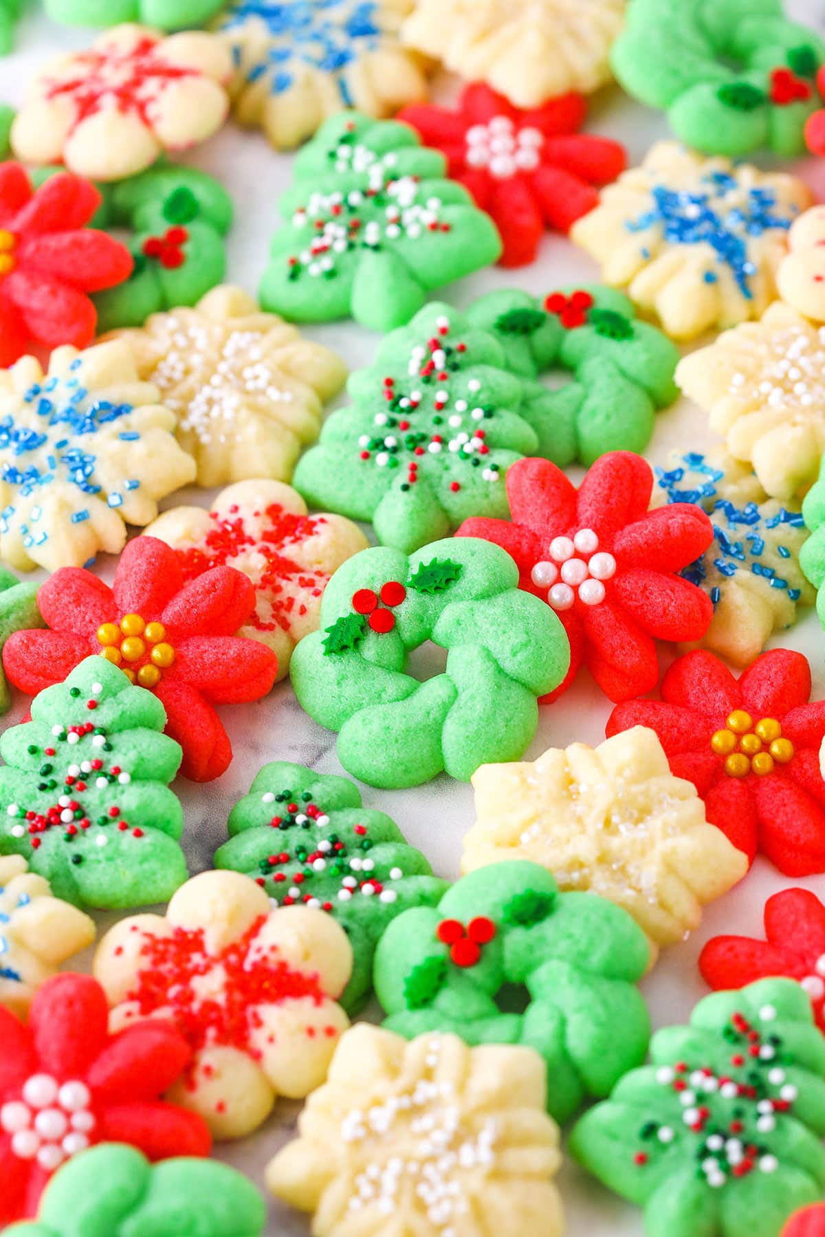 Red flower, white snowflake and green Christmas tree Spritz Cookies spread out over a white table top