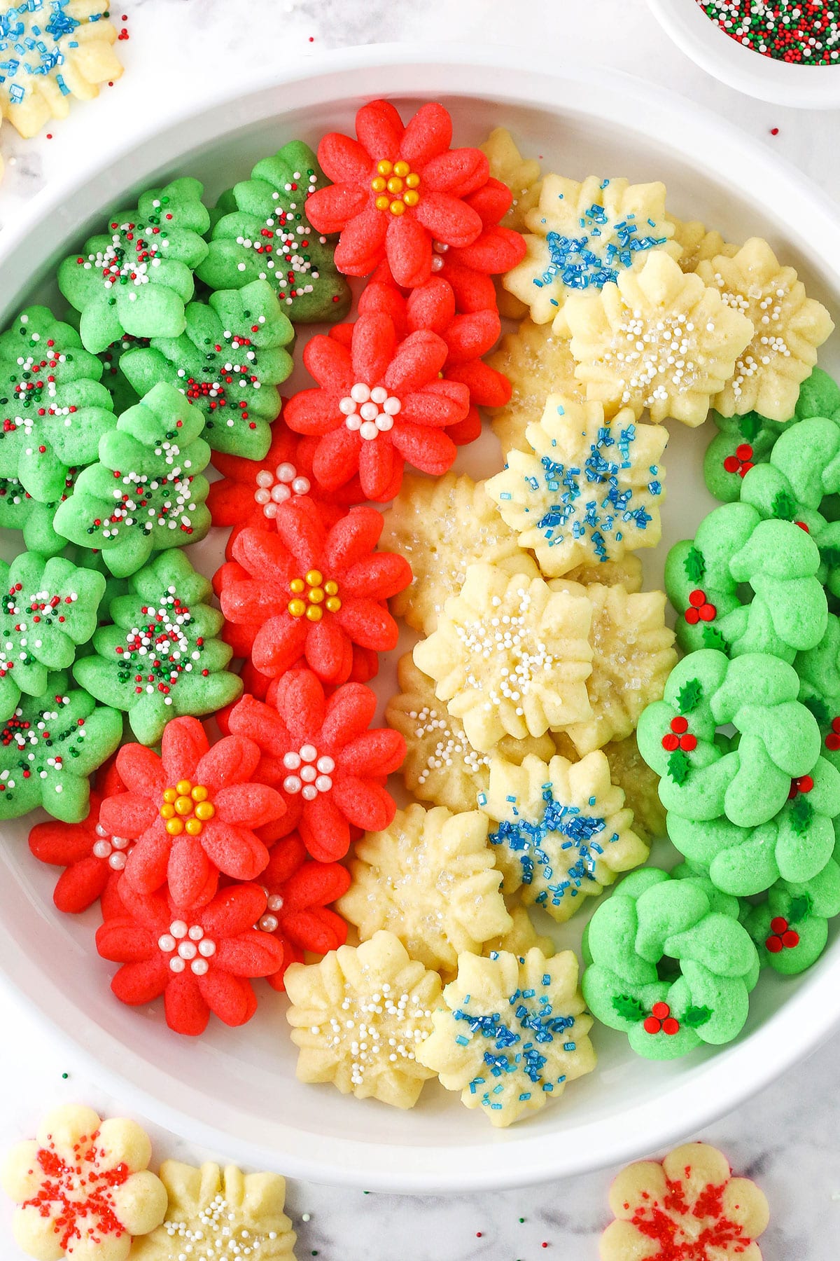 Red flower, white snowflake and green Christmas tree Spritz Cookies layered in a white cookie platter