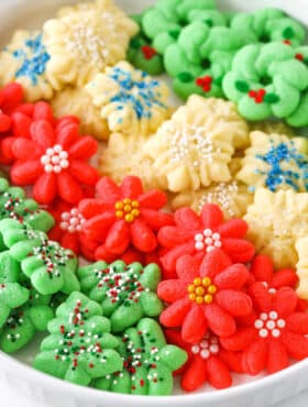 Red flower, white snowflake and green Christmas tree Spritz Cookies layered in a white cookie platter