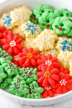 Red flower, white snowflake and green Christmas tree Spritz Cookies layered in a white cookie platter