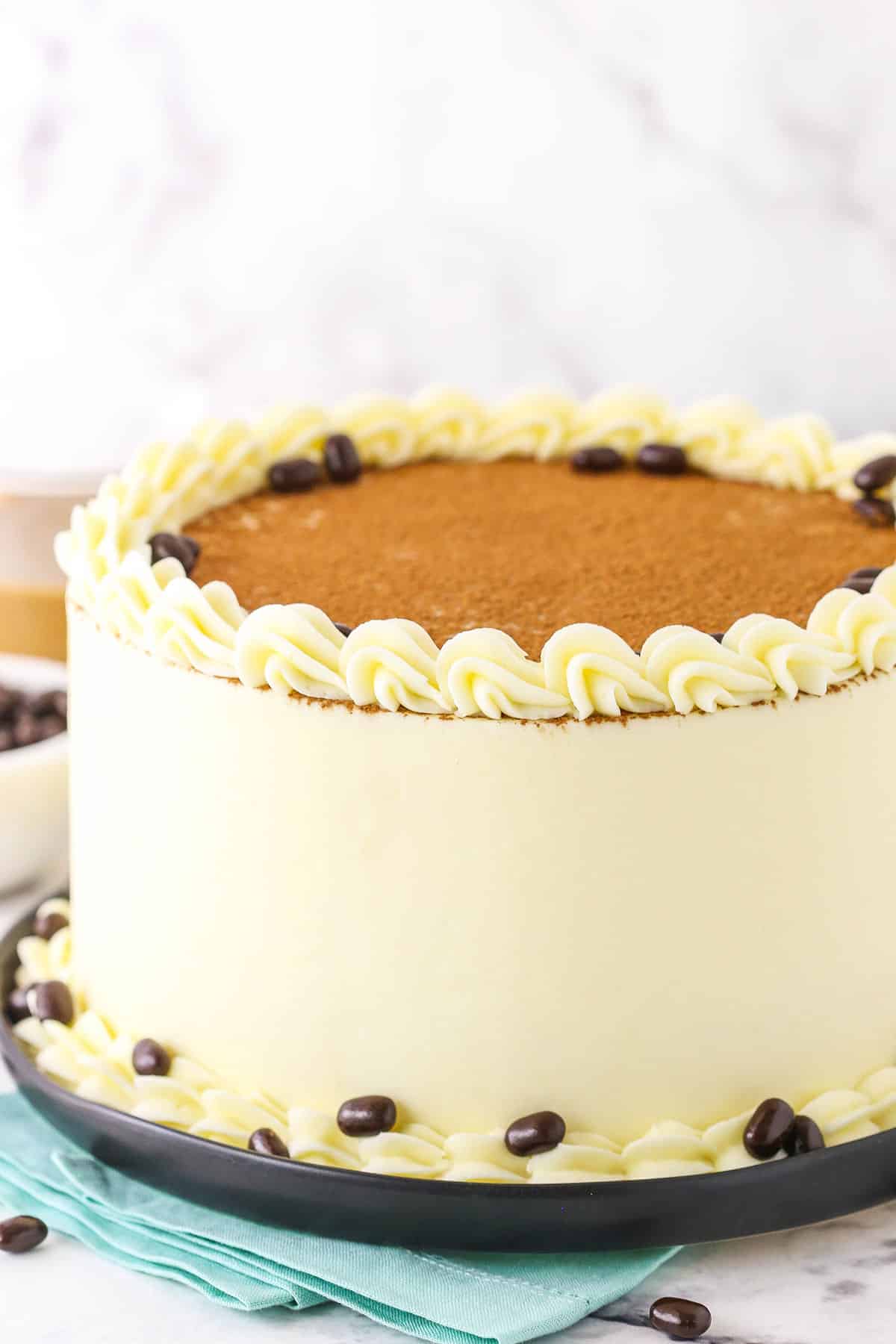 Side view of a full Tiramisu Layer Cake on a black plate