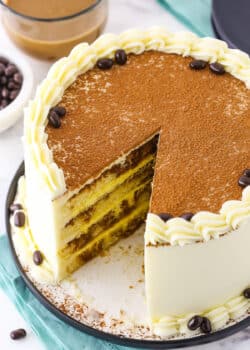 Overhead view of a full Tiramisu Layer Cake with a slice removed on a black plate