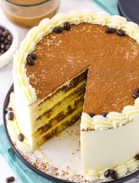 Overhead view of a full Tiramisu Layer Cake with a slice removed on a black plate