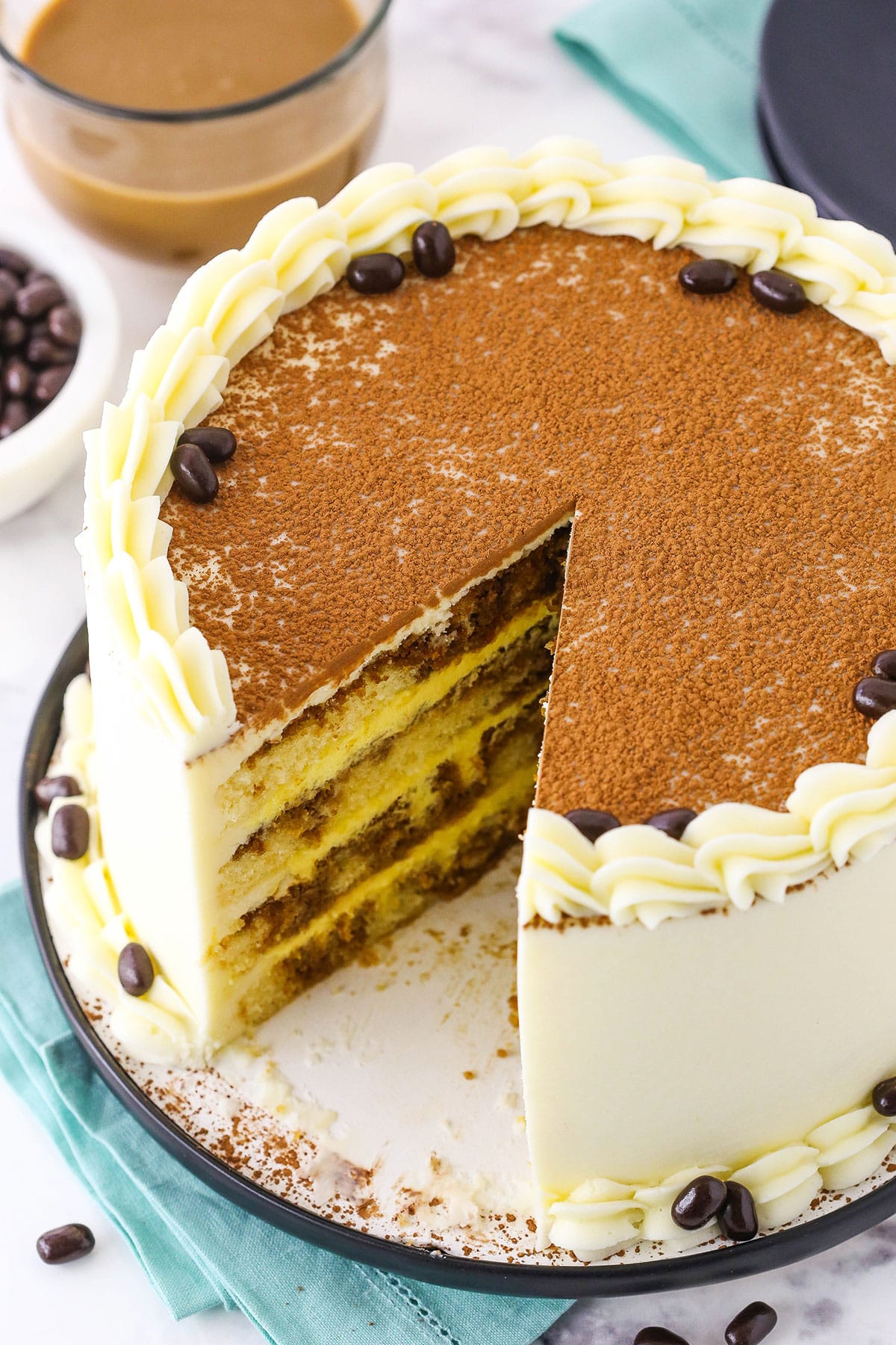 Overhead view of a full Tiramisu Layer Cake with a slice removed on a black plate