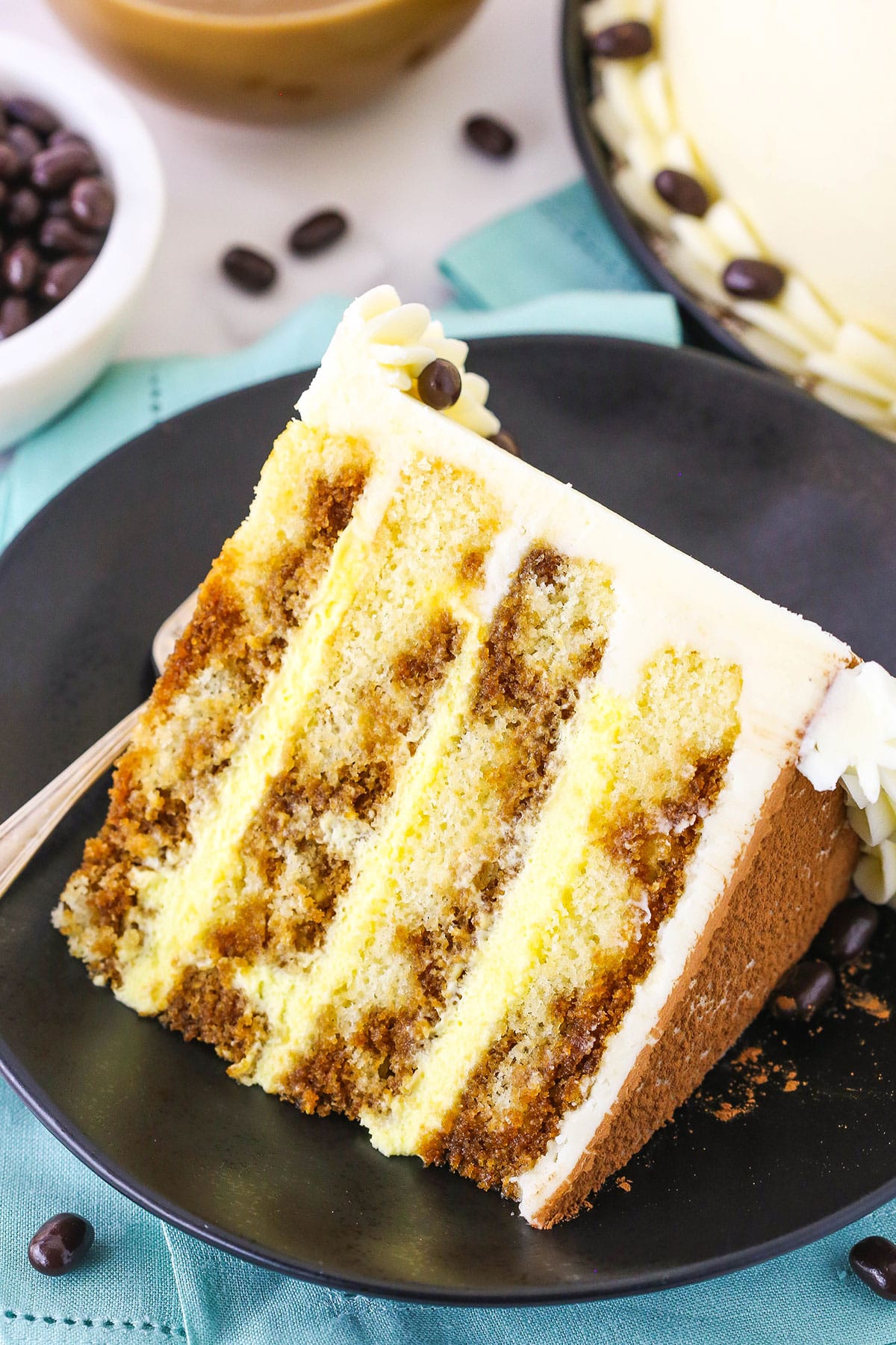 A slice of Tiramisu Layer Cake on a black plate with a fork