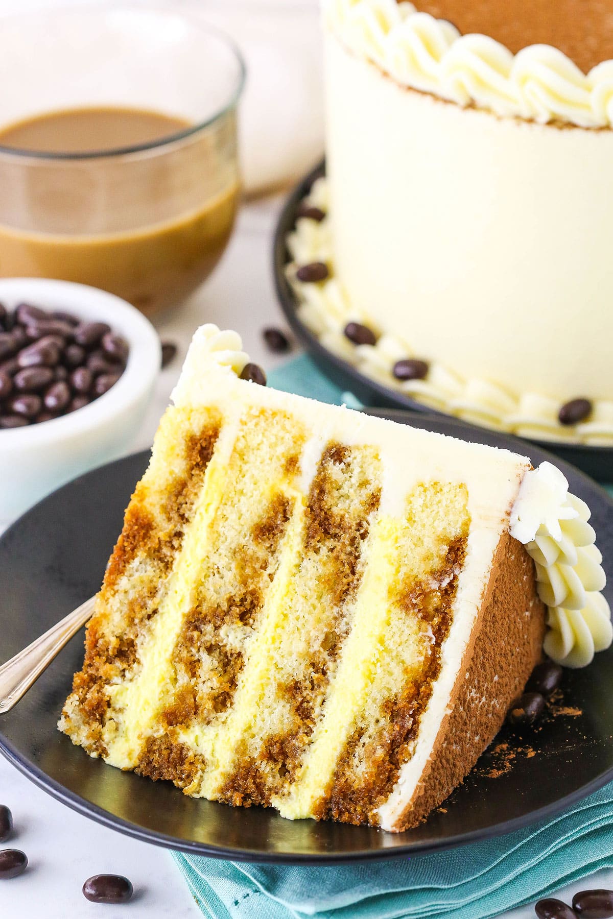 A slice of Tiramisu Layer Cake on a black plate with a fork