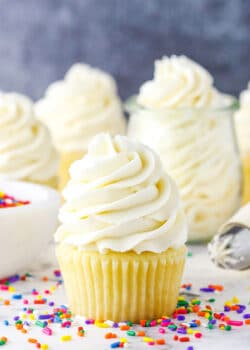 Vanilla Buttercream Frosting piped onto a vanilla cupcake surrounded by multicolored sprinkles