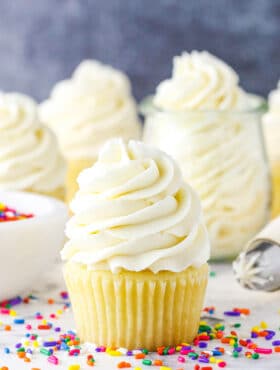 Vanilla Buttercream Frosting piped onto a vanilla cupcake surrounded by multicolored sprinkles