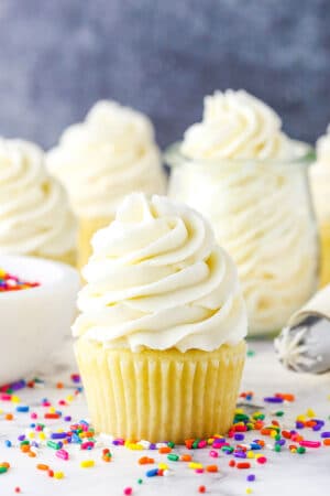 Vanilla Buttercream Frosting piped onto a vanilla cupcake surrounded by multicolored sprinkles