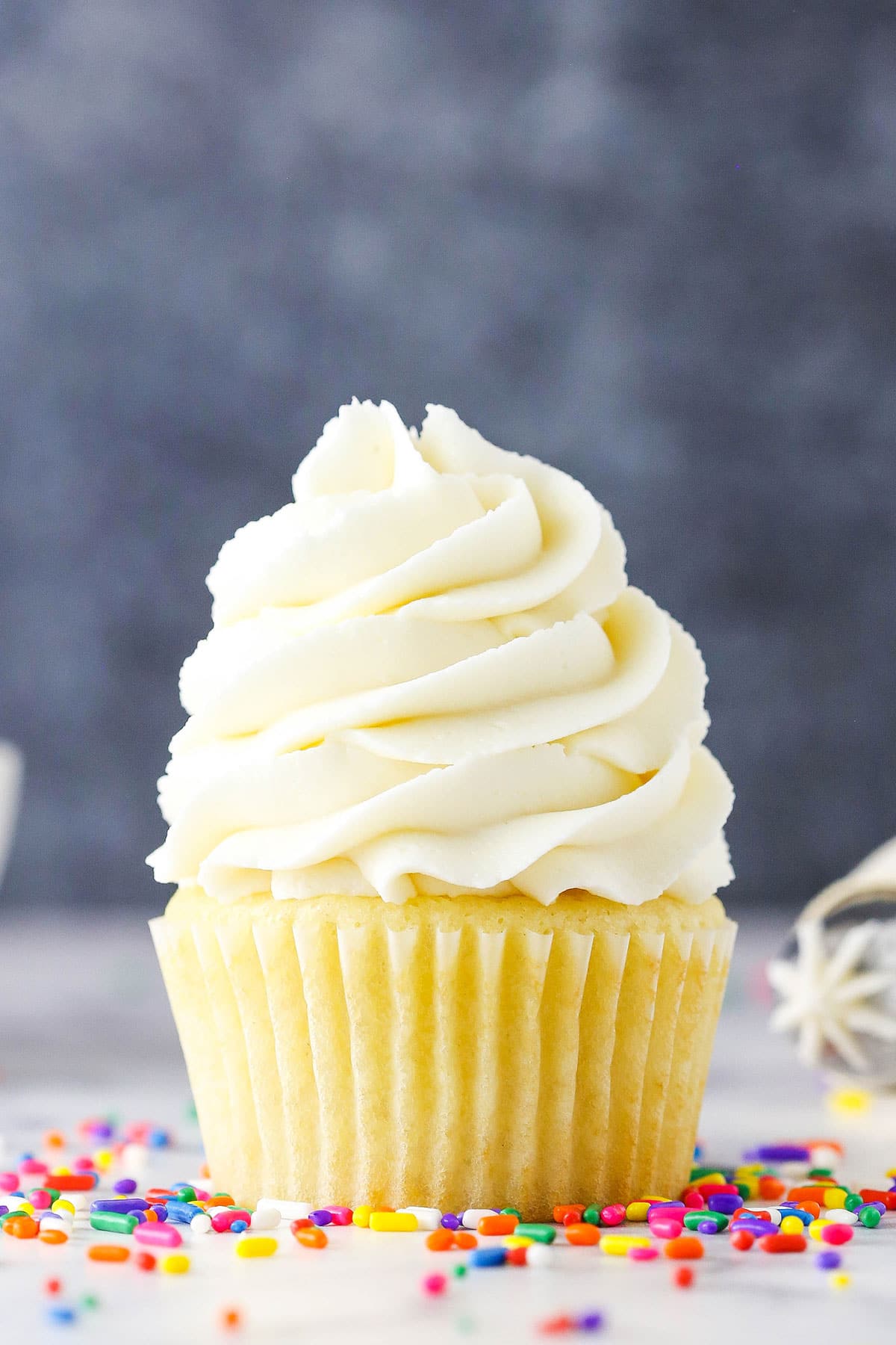 Vanilla Buttercream Frosting piped onto a vanilla cupcake surrounded by multicolored sprinkles