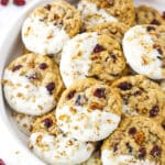 White Chocolate Dipped Cranberry Oatmeal Cookies coated with chopped pecans layered in a white serving platter with a small dish of dried cranberries in the background