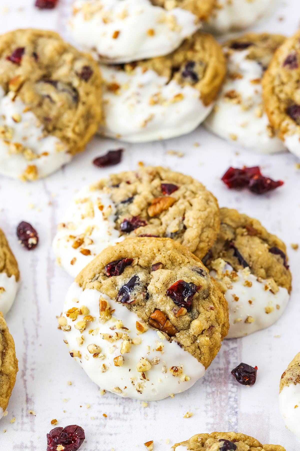 Three White Chocolate Dipped Cranberry Oatmeal Cookies layered with more White Chocolate Dipped Cranberry Oatmeal Cookies in the background on a white table top