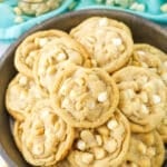 White Chocolate Macadamia Nut Cookies stacked in a dark platter with white chocolate chips and macadamia nuts in the background