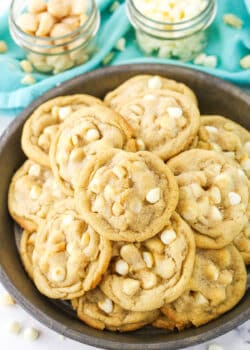 White Chocolate Macadamia Nut Cookies stacked in a dark platter with white chocolate chips and macadamia nuts in the background