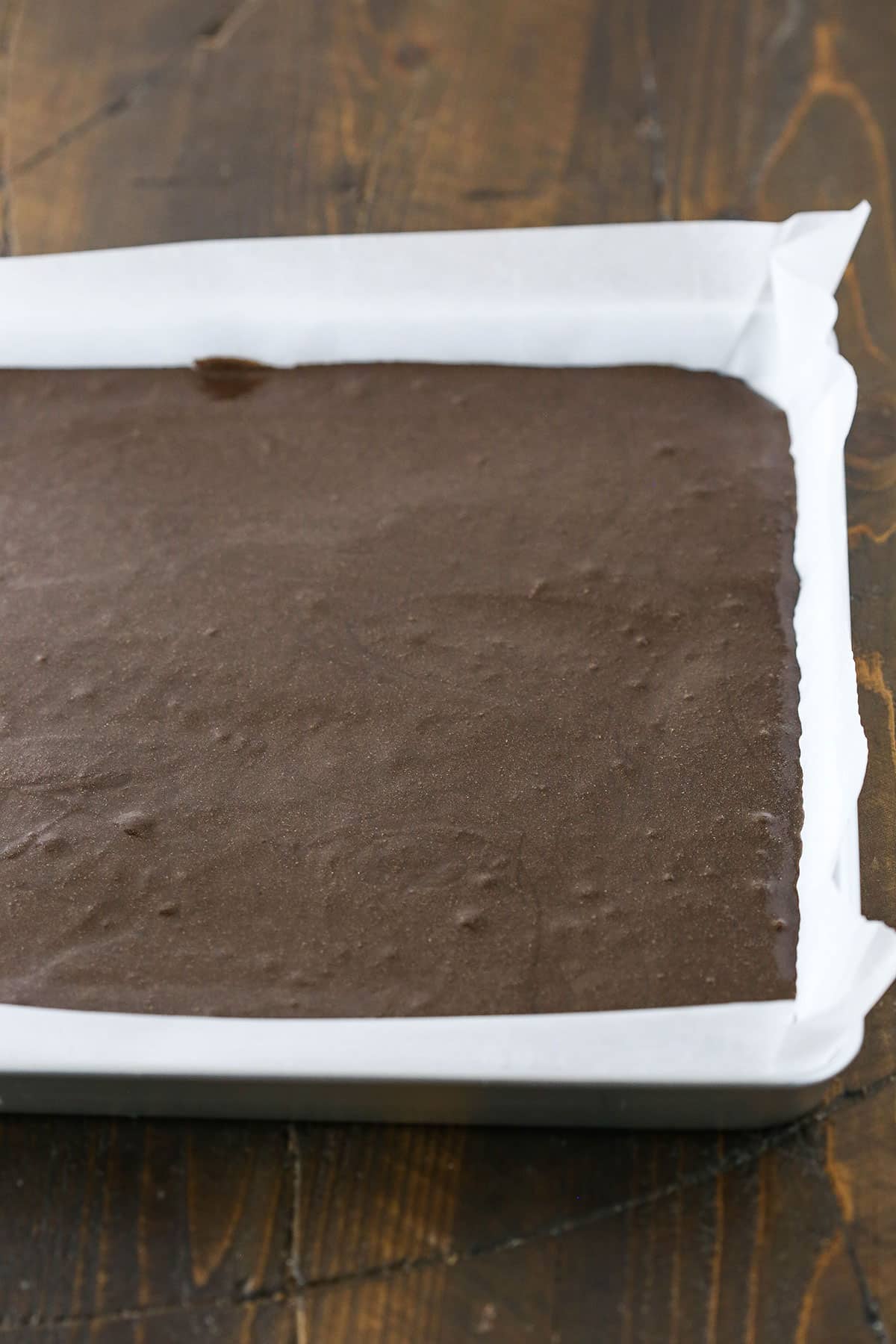 A step in making a Yule Log Cake showing the chocolate cake batter poured into a sheet pan lined with parchment paper.