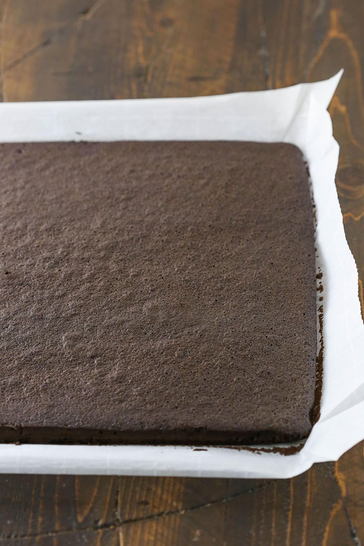 A step in making a Yule Log Cake showing the chocolate cake baked in a sheet pan lined with parchment paper.