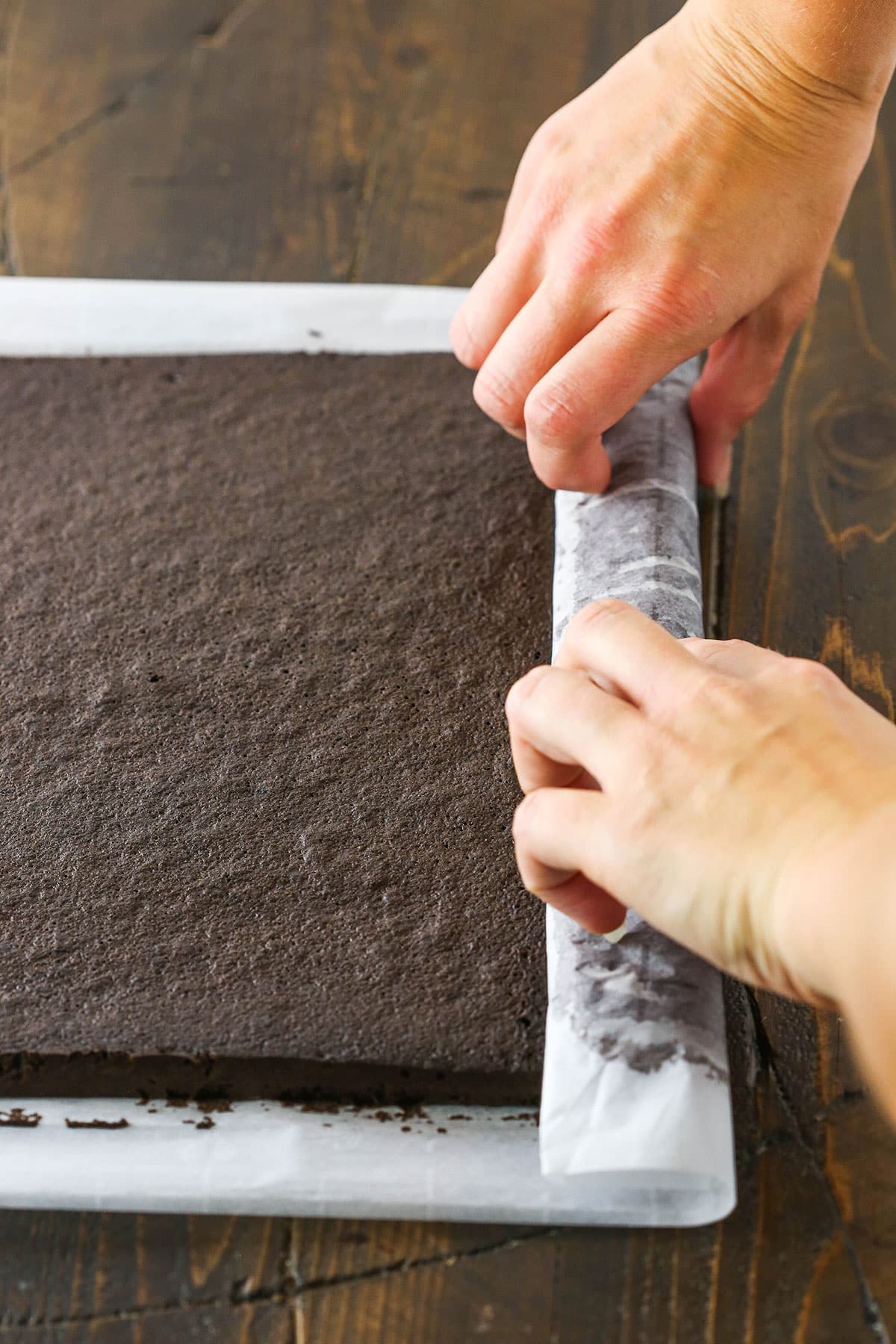 A step in making a Yule Log Cake showing the baked chocolate cake removed from the sheet pan and being rolled