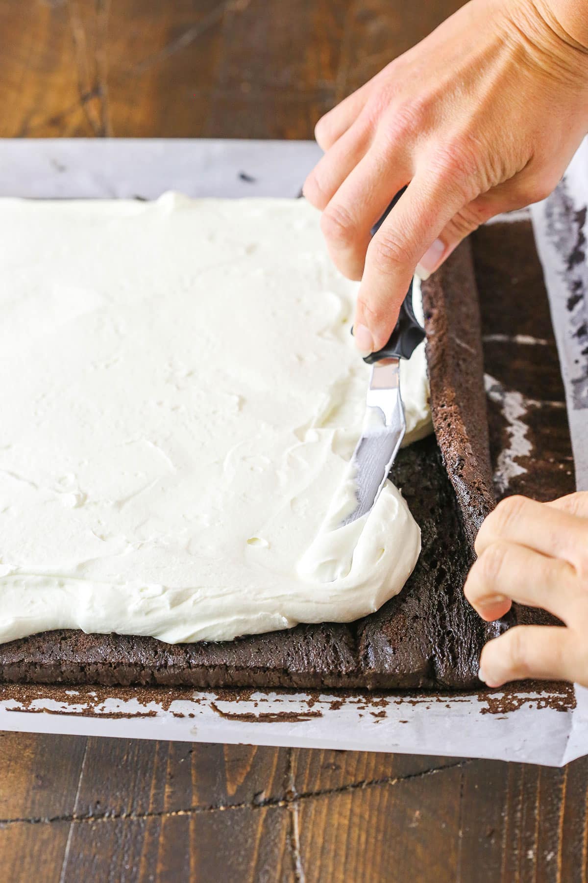 A step in making a Yule Log Cake showing evenly spreading the mascarpone whipped cream filling over the unrolled baked chocolate cake.