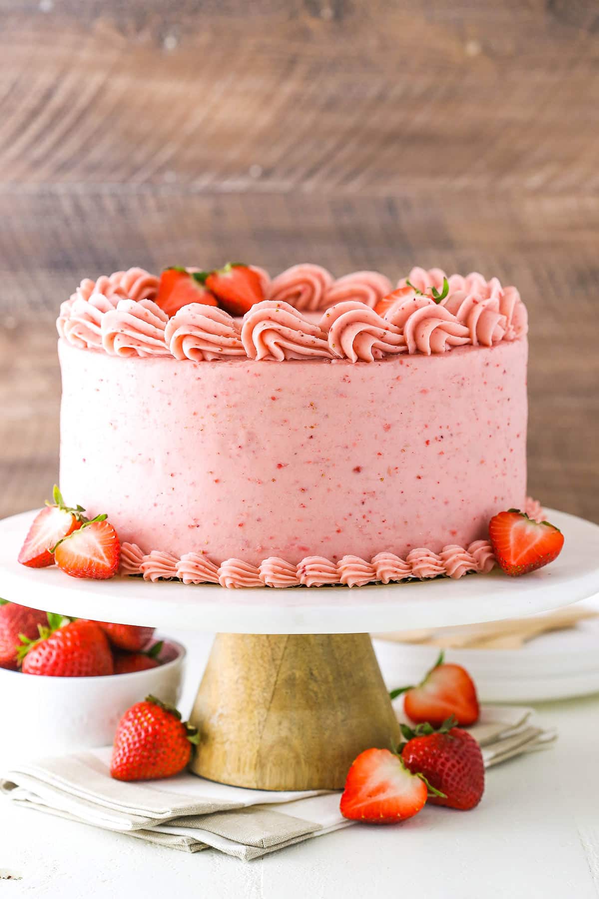 Homemade strawberry cake on a cake stand near fresh strawberries.