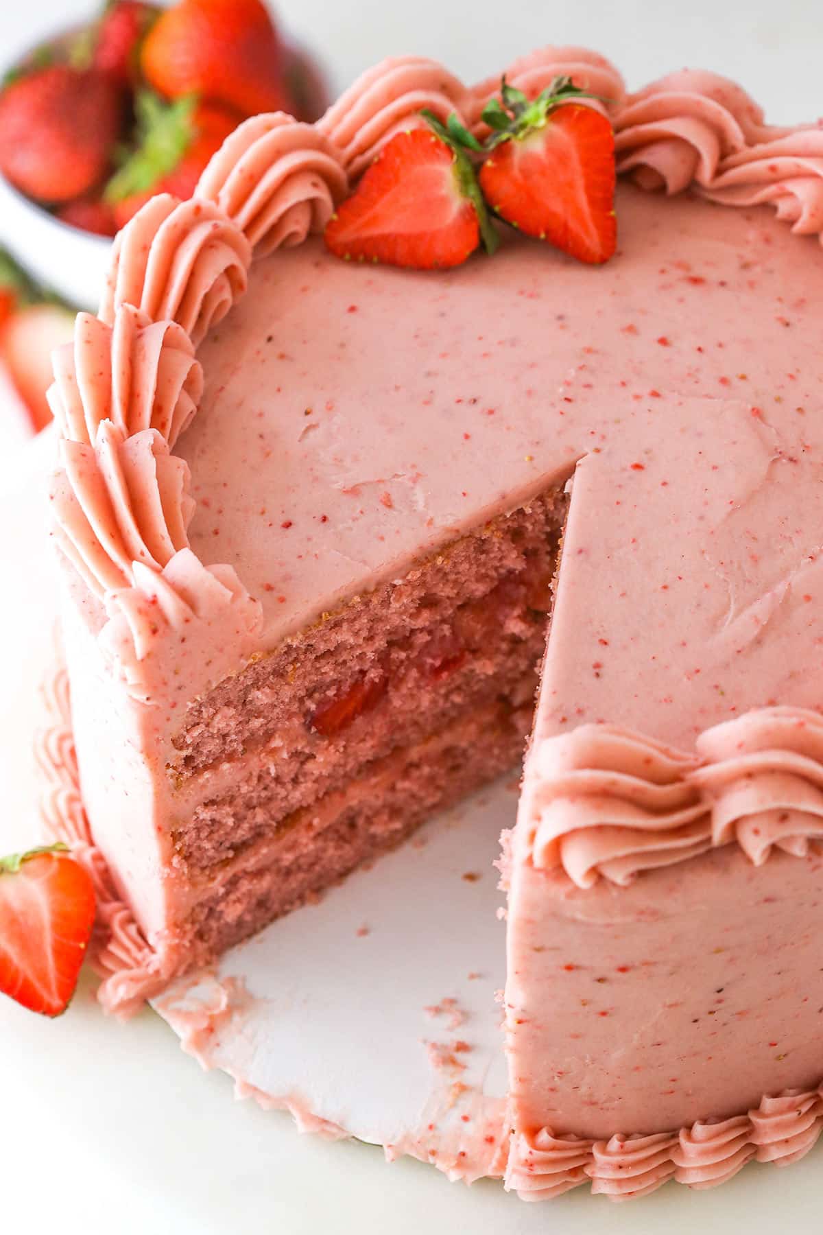 Homemade strawberry cake with a slice taken out of it near fresh strawberries.