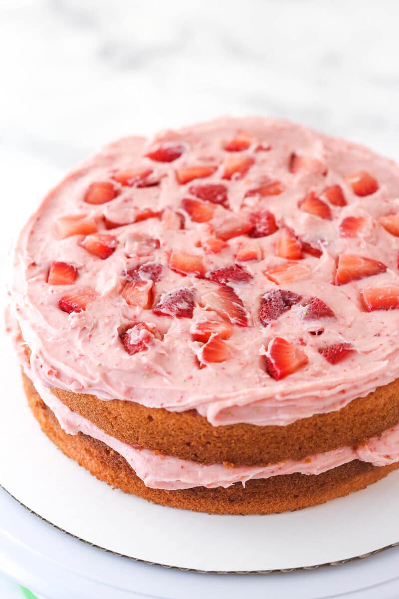 Adding chopped strawberries to the second layer of cake and frosting in homemade strawberry cake.