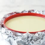 a cheesecake in a springform pan wrapped in slow cooker bag and aluminum foil for a water bath