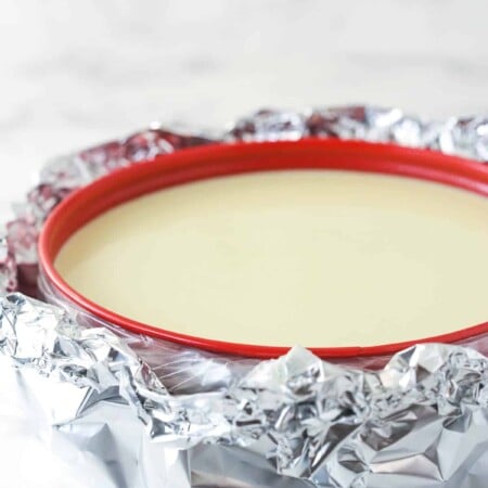 a cheesecake in a springform pan wrapped in slow cooker bag and aluminum foil for a water bath