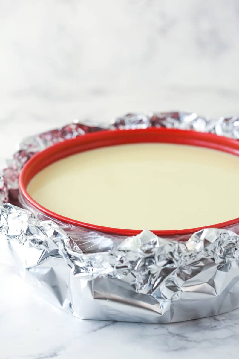a cheesecake in a springform pan wrapped in slow cooker bag and aluminum foil for a water bath