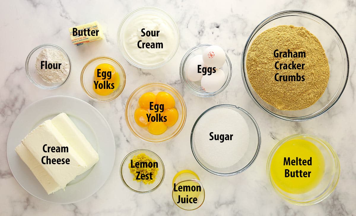 Lemon cheesecake is perfect for summer. Creamy lemon cheesecake filling is baked into sweet Graham cracker crust and topped with lemon curd. Ingredients for lemon cheesecake separated into bowls.