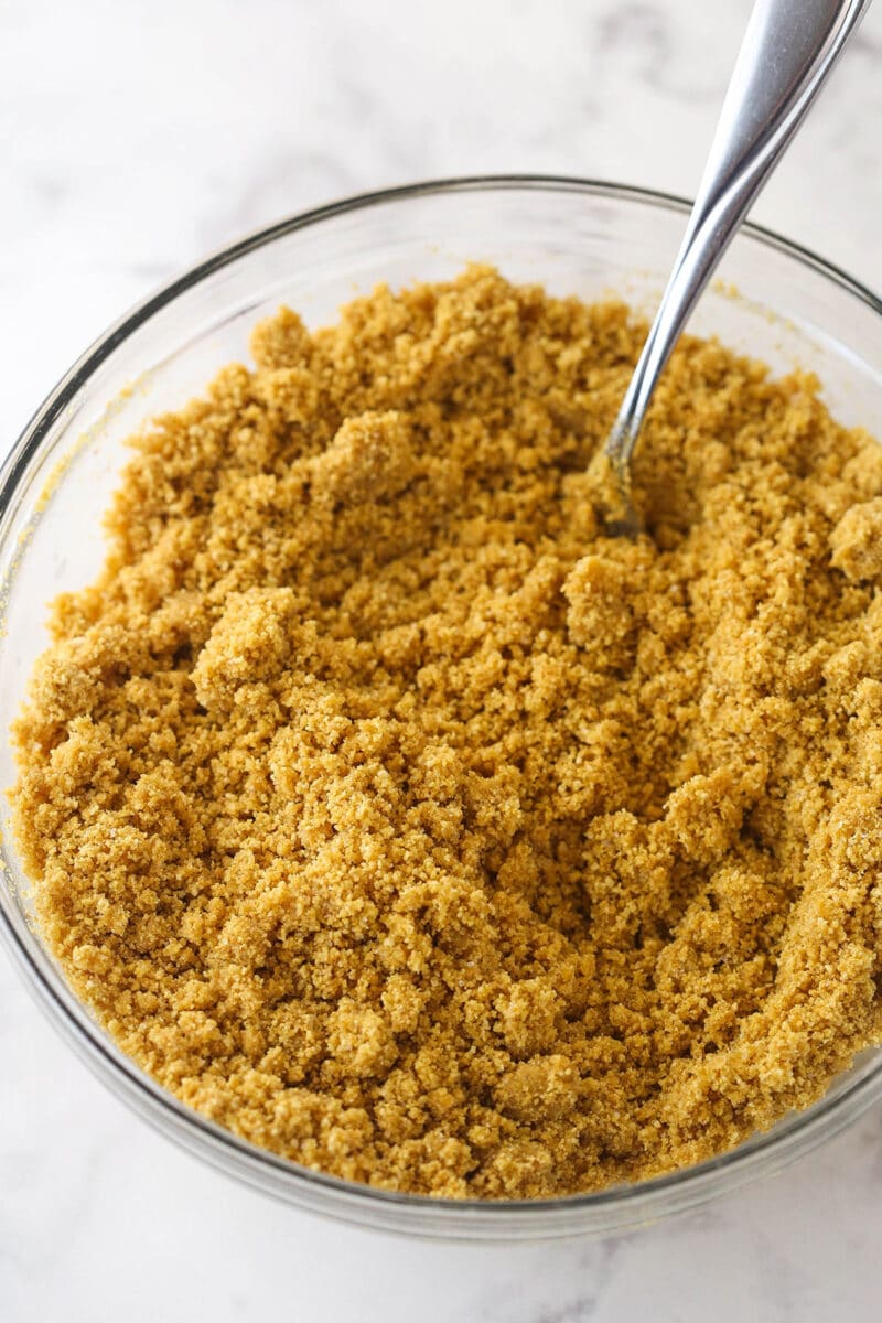 Lemon cheesecake is perfect for summer. Creamy lemon cheesecake filling is baked into sweet Graham cracker crust and topped with lemon curd. Mixing together Graham cracker crumbles and melted butter for Graham cracker crust.