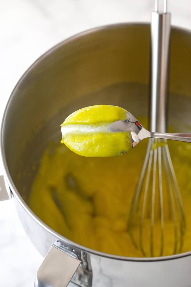 A spoon with lemon curd on it. A finger has been traced through the lemon curd to show its thickness.