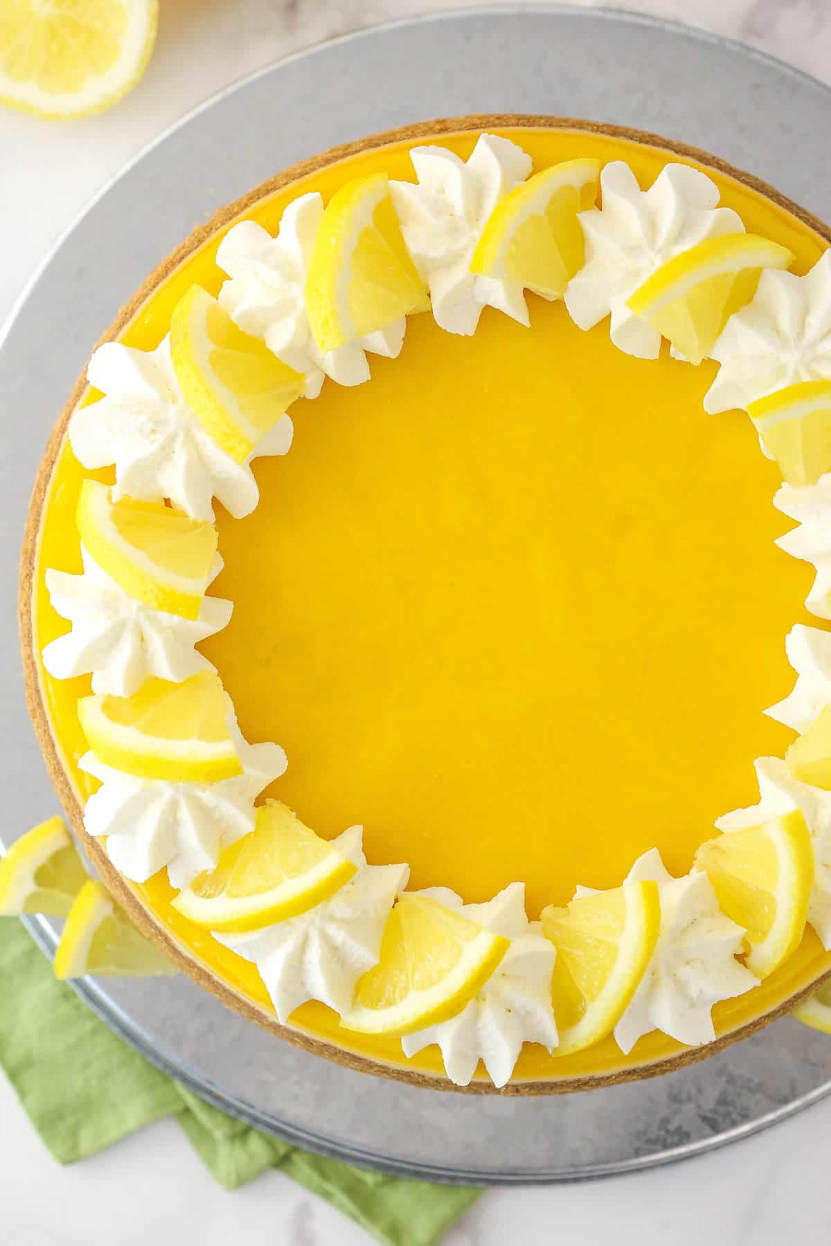 Lemon cheesecake is perfect for summer. Creamy lemon cheesecake filling is baked into sweet Graham cracker crust and topped with lemon curd. Overhead of a whole lemon cheesecake.