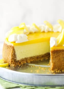 Lemon cheesecake on a cake platter with a slice taken out of it.