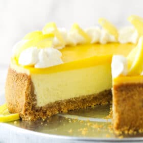 Lemon cheesecake on a cake platter with a slice taken out of it.