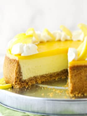 Lemon cheesecake on a cake platter with a slice taken out of it.