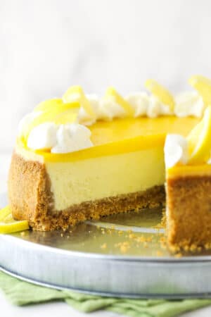 Lemon cheesecake on a cake platter with a slice taken out of it.