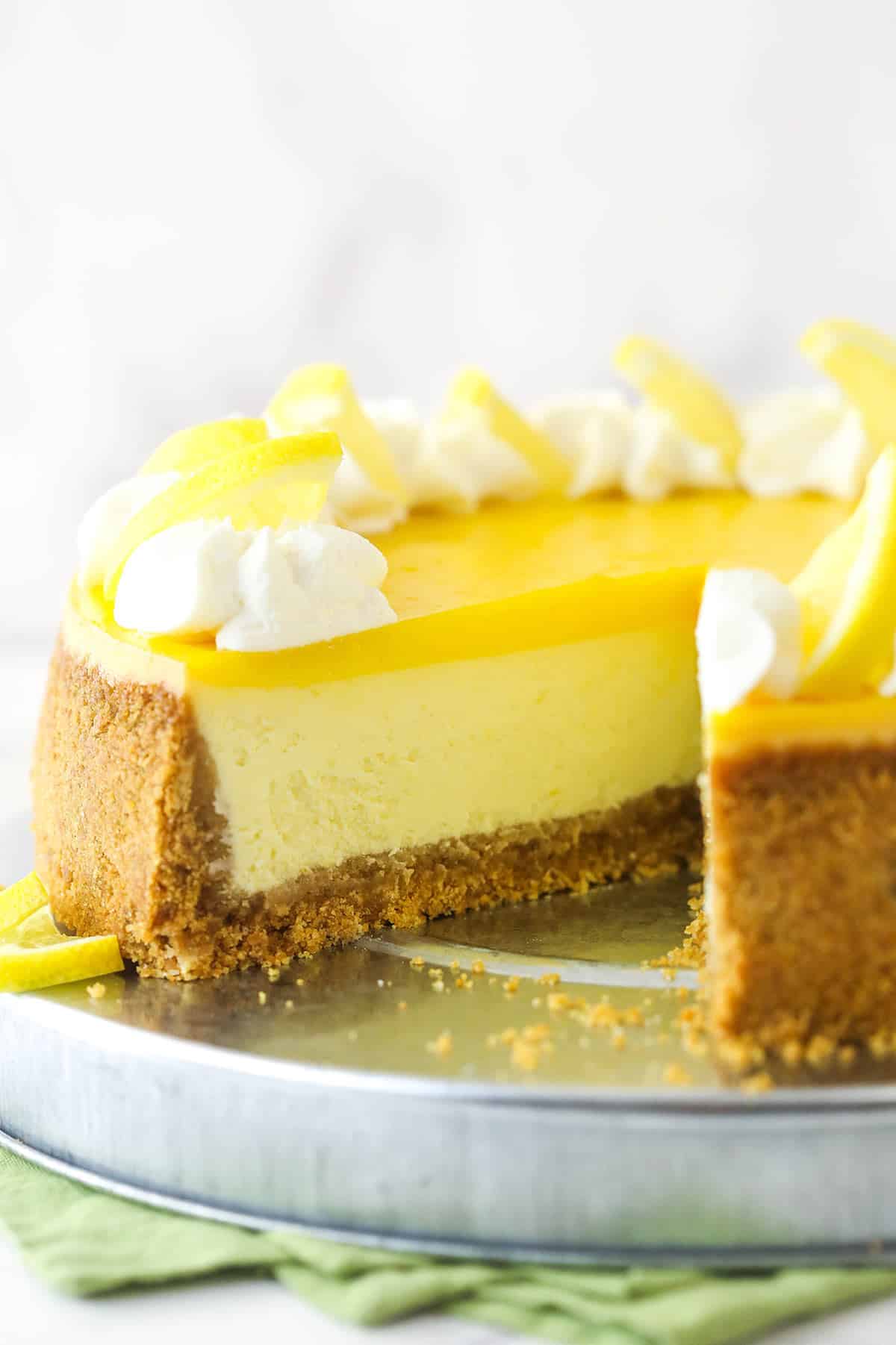 Lemon cheesecake on a cake platter with a slice taken out of it.