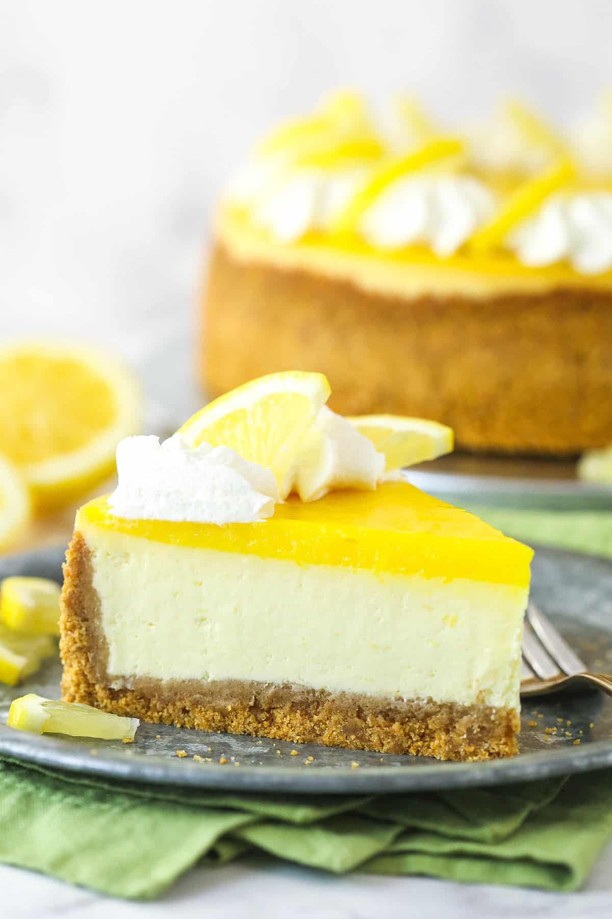 Lemon cheesecake is perfect for summer. Creamy lemon cheesecake filling is baked into sweet Graham cracker crust and topped with lemon curd. Lemon cheesecake served on a plate.