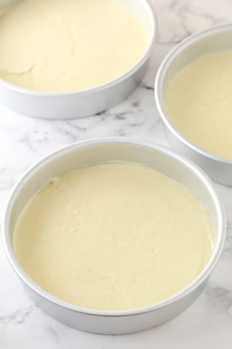 Vanilla cake batter divided between 3 cake pans ready to be baked.