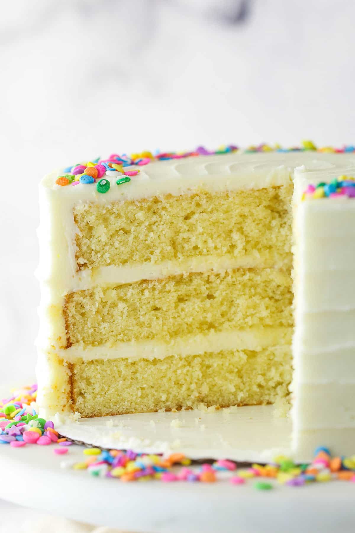 This moist vanilla layer cake is made of three layers of moist vanilla cake that are filled and frosted with rich vanilla buttercream. Moist vanilla layer cake with a slice taken out of it.