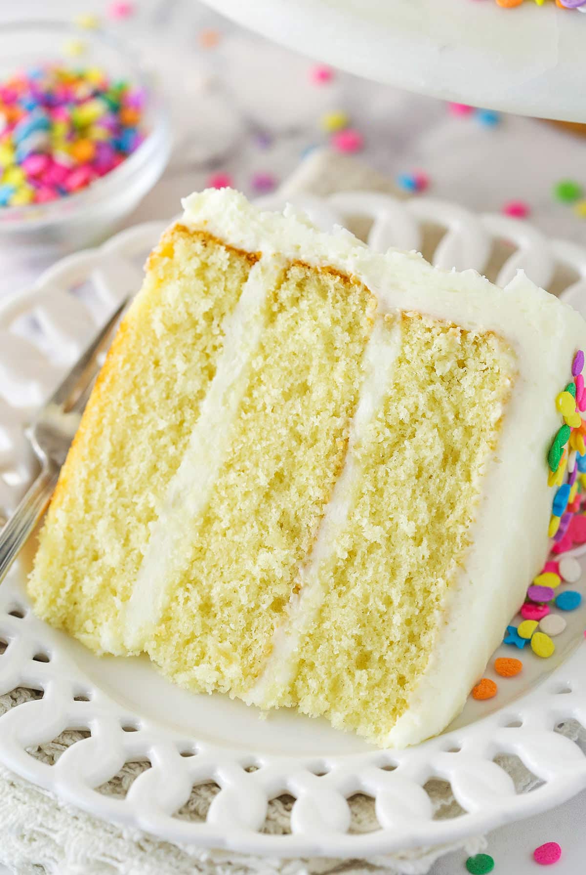 A slice of moist vanilla layer cake on a plate with a fork.