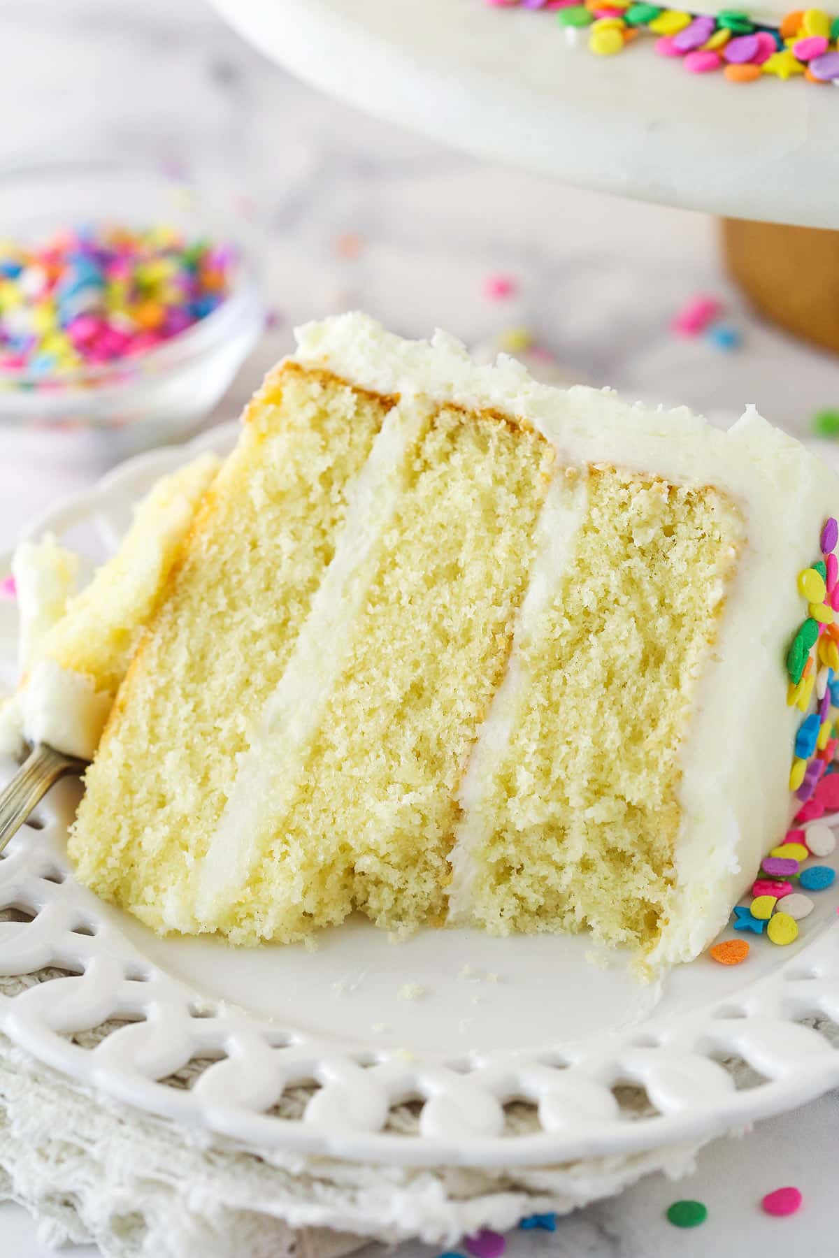 A slice of moist vanilla layer cake on a plate with a bite taken out of it.