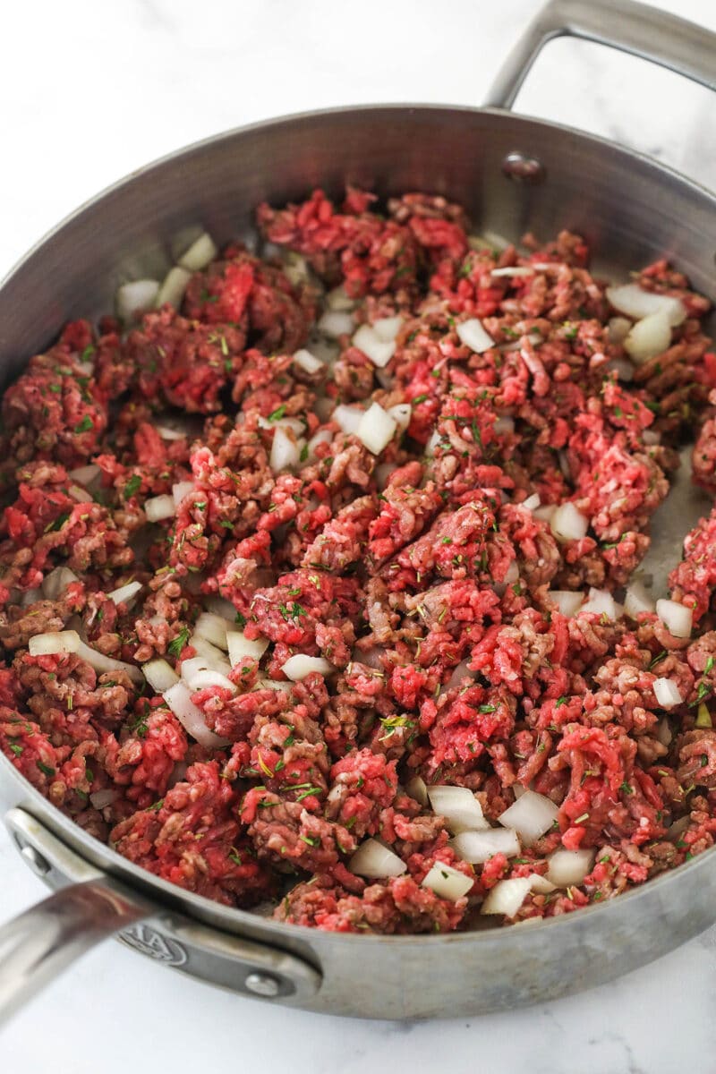 This easy Sheperd's Pie is made of perfectly seasoned ground beef and veggies topped with mashed potatoes and cheese and baked to bubbly. Cooking ground beef and onions with herbs in a pan.