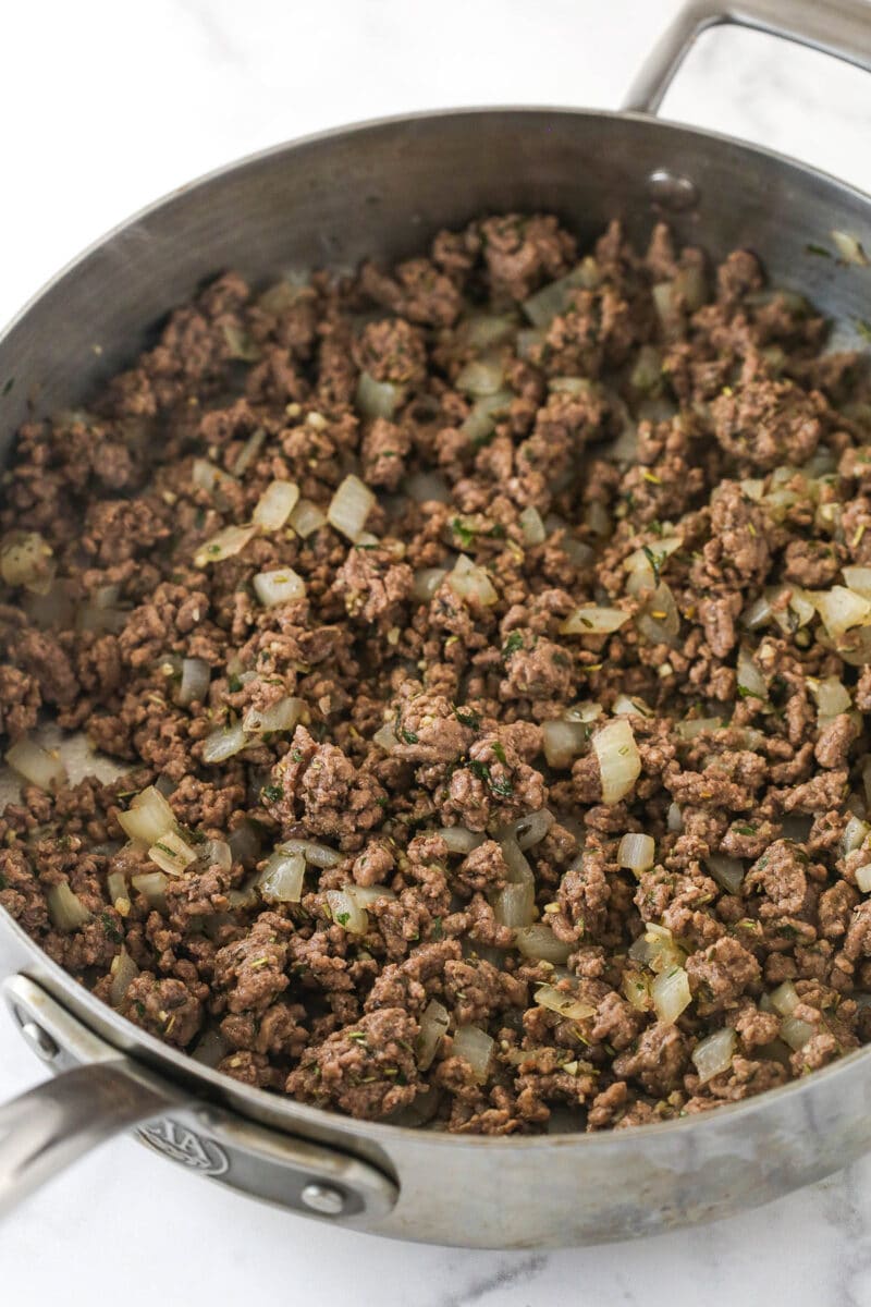 Ground beef cooked with onions and herbs in a pan.