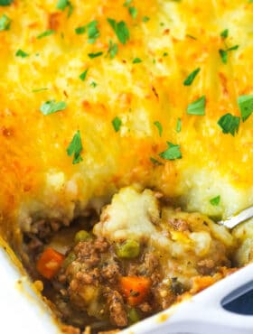 Shepherd's pie in a baking dish with a serving spoon taking a piece out of it.