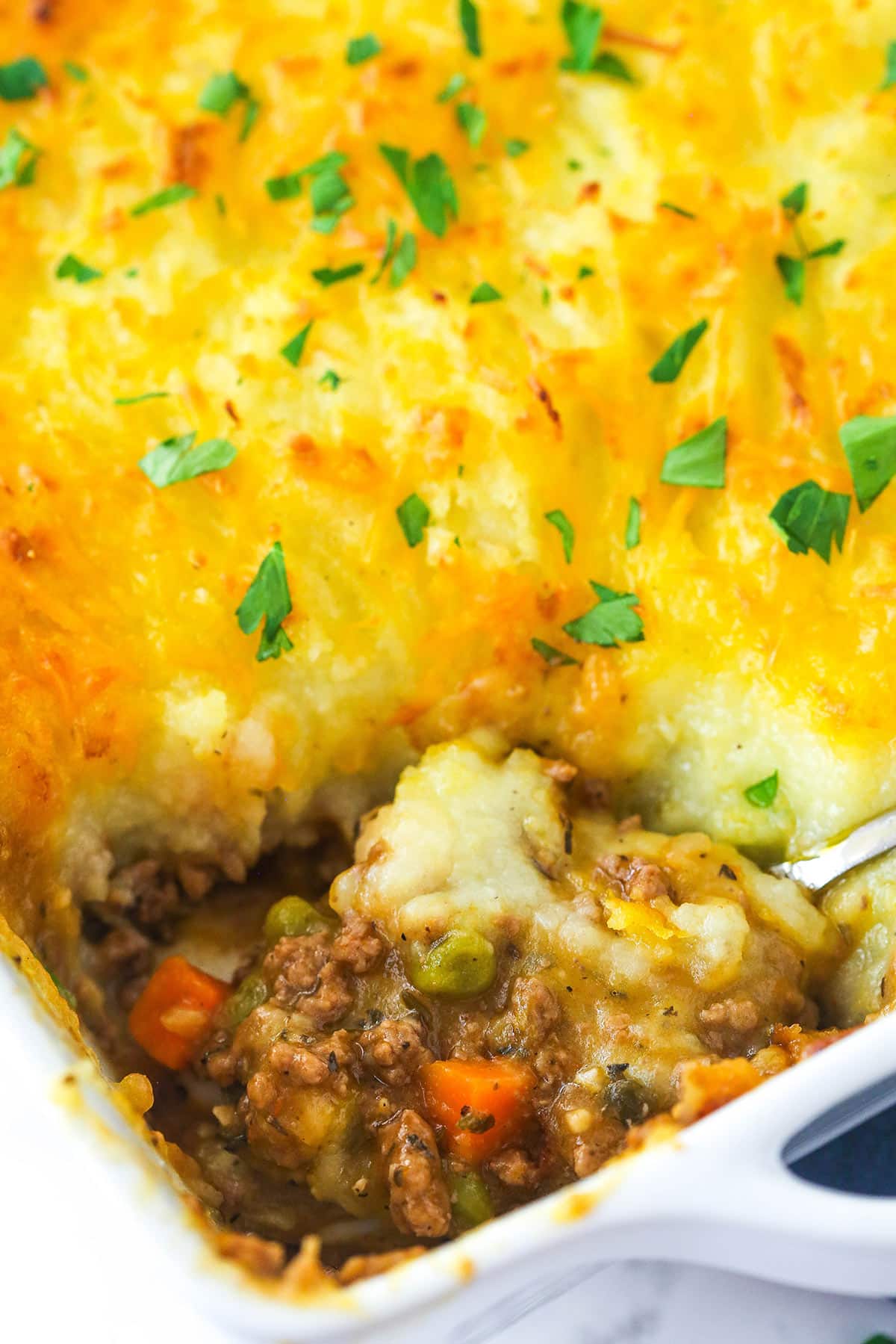 Shepherd's pie in a baking dish with a serving spoon taking a piece out of it.